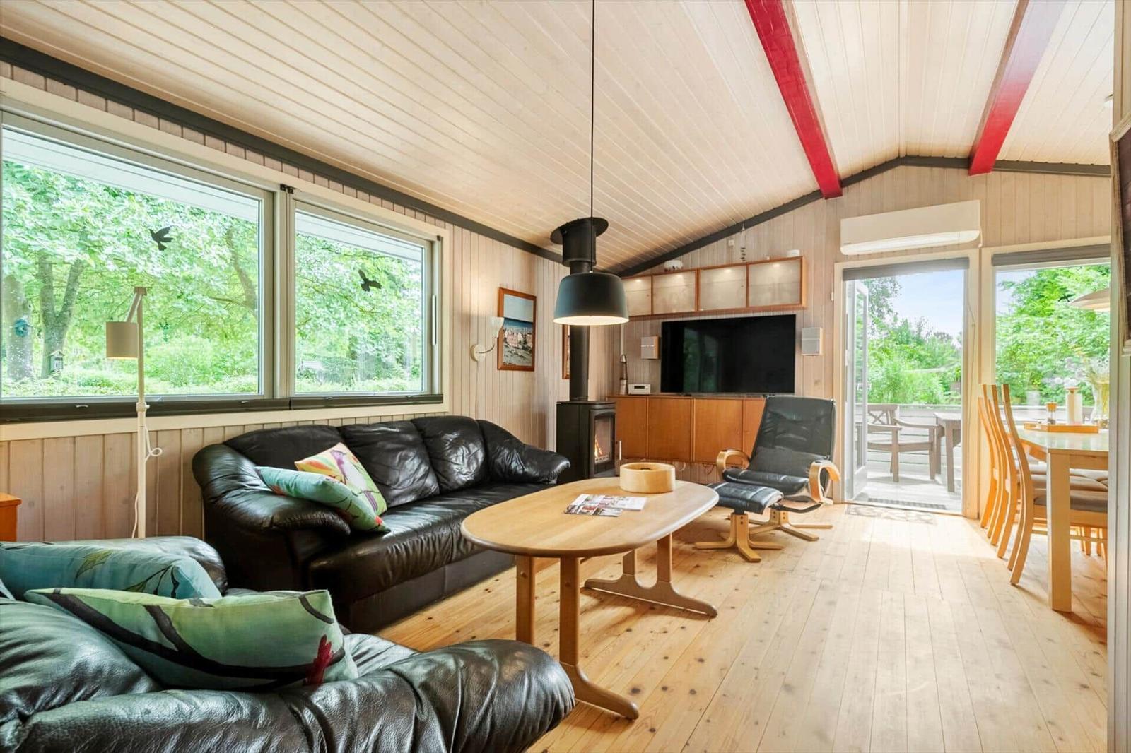 Wohnzimmer mit Ledersofa, Holztisch und Kamin. Durchgänge zu Terrasse und Garten.