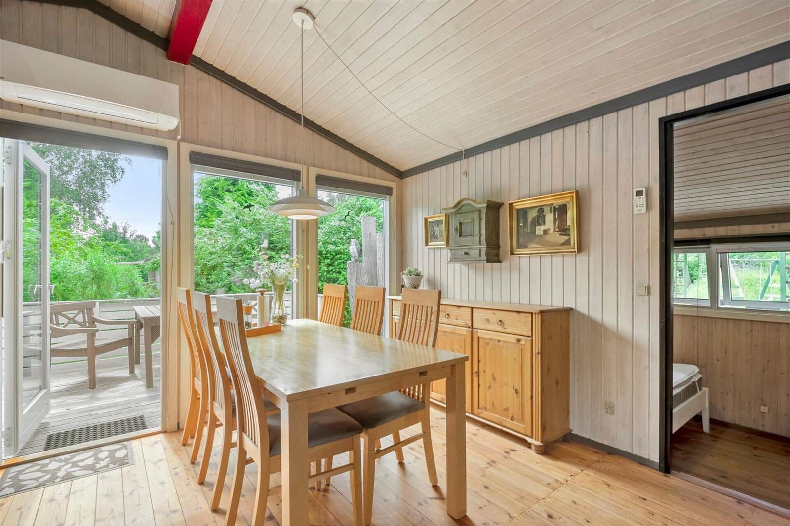 Essbereich mit Tisch, Stühlen und Blick auf Balkon. Holzwände und -boden. Schlafzimmer im Hintergrund.