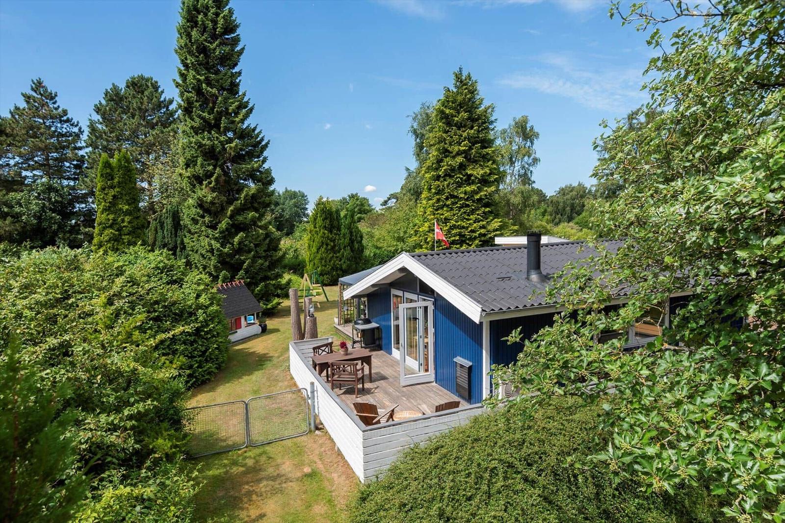 Blau gestrichenes Haus mit Terrasse, Grill und Garten. Umgeben von Bäumen und Sträuchern.