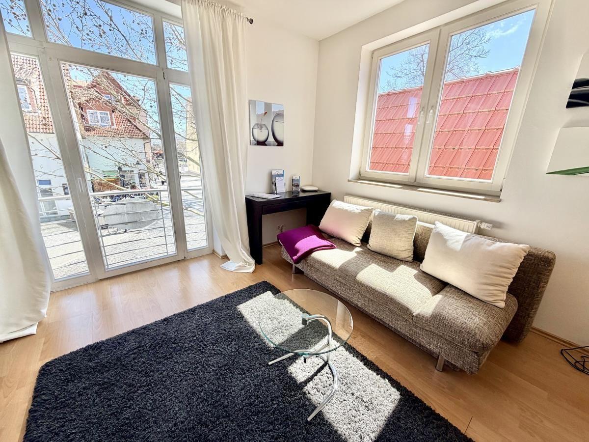 Wohnzimmer mit Sofa, Glas-Tisch und Blick auf die Straße durch Glastür.