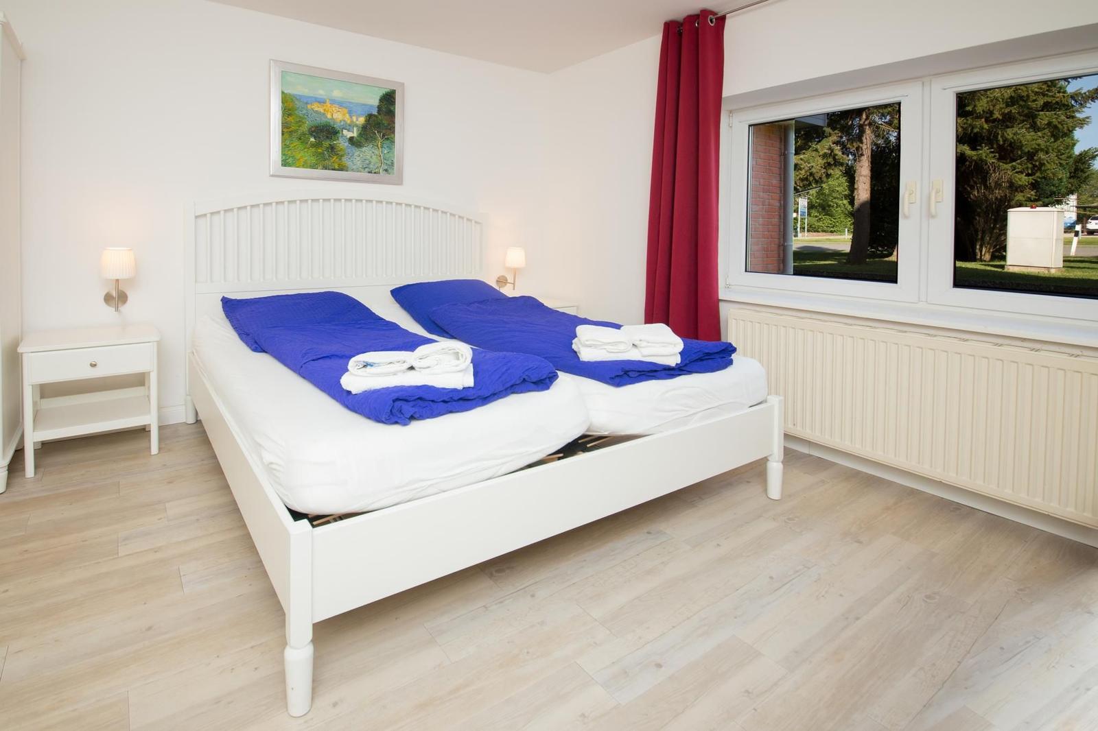 Schlafzimmer mit Doppelbett, roten Vorhängen und Fensterblick auf Grünflächen.