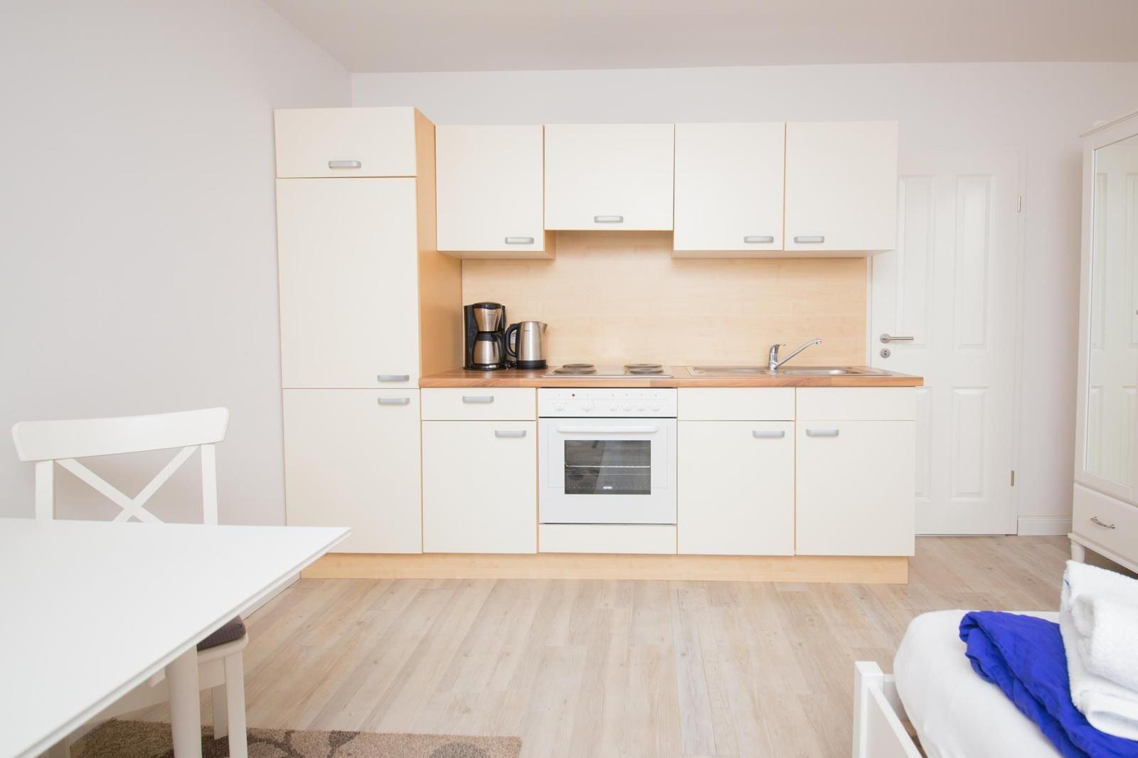 Küche mit weißen Schränken, Herd und Spüle. Holzfußboden und weißer Tisch mit Stuhl.
