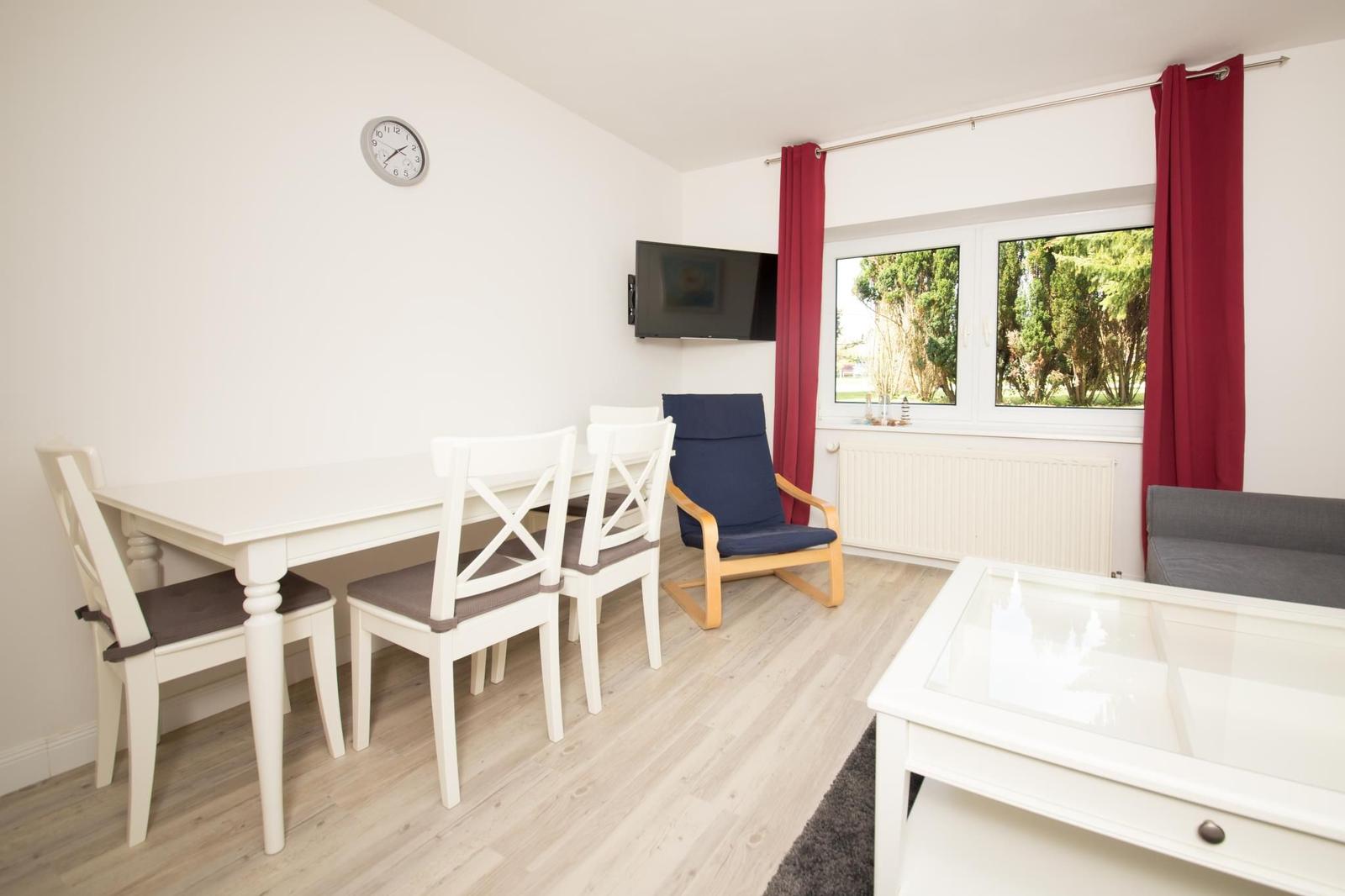 Essbereich mit Tisch, Stühlen, Fernseher und Fenster mit Blick auf Grünfläche.