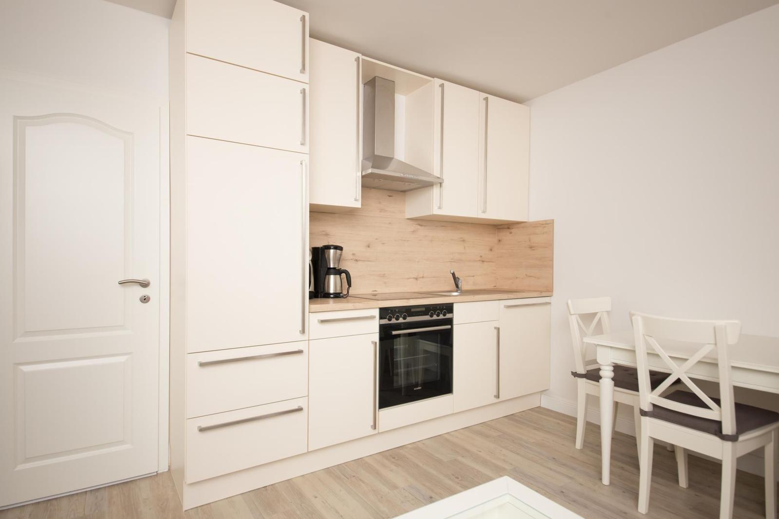Küche mit weißen Schränken, Holzrückwand und Essbereich mit Tisch und Stühlen.