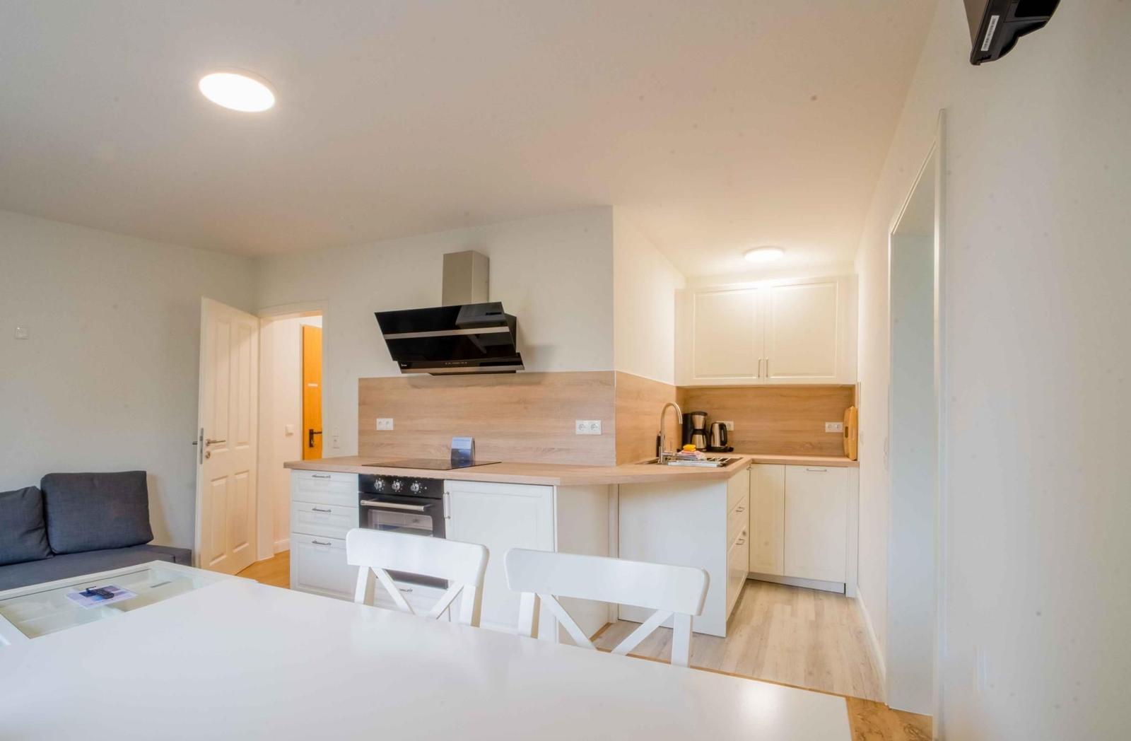 Küche mit Arbeitsplatte, Herd und Spüle. Essbereich mit Tisch und Stühlen. Wohnbereich mit Sofa.