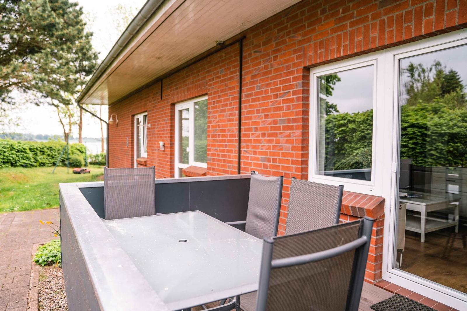 Terrasse mit Tisch und Stühlen vor einem roten Backsteinhaus mit Fenstern.