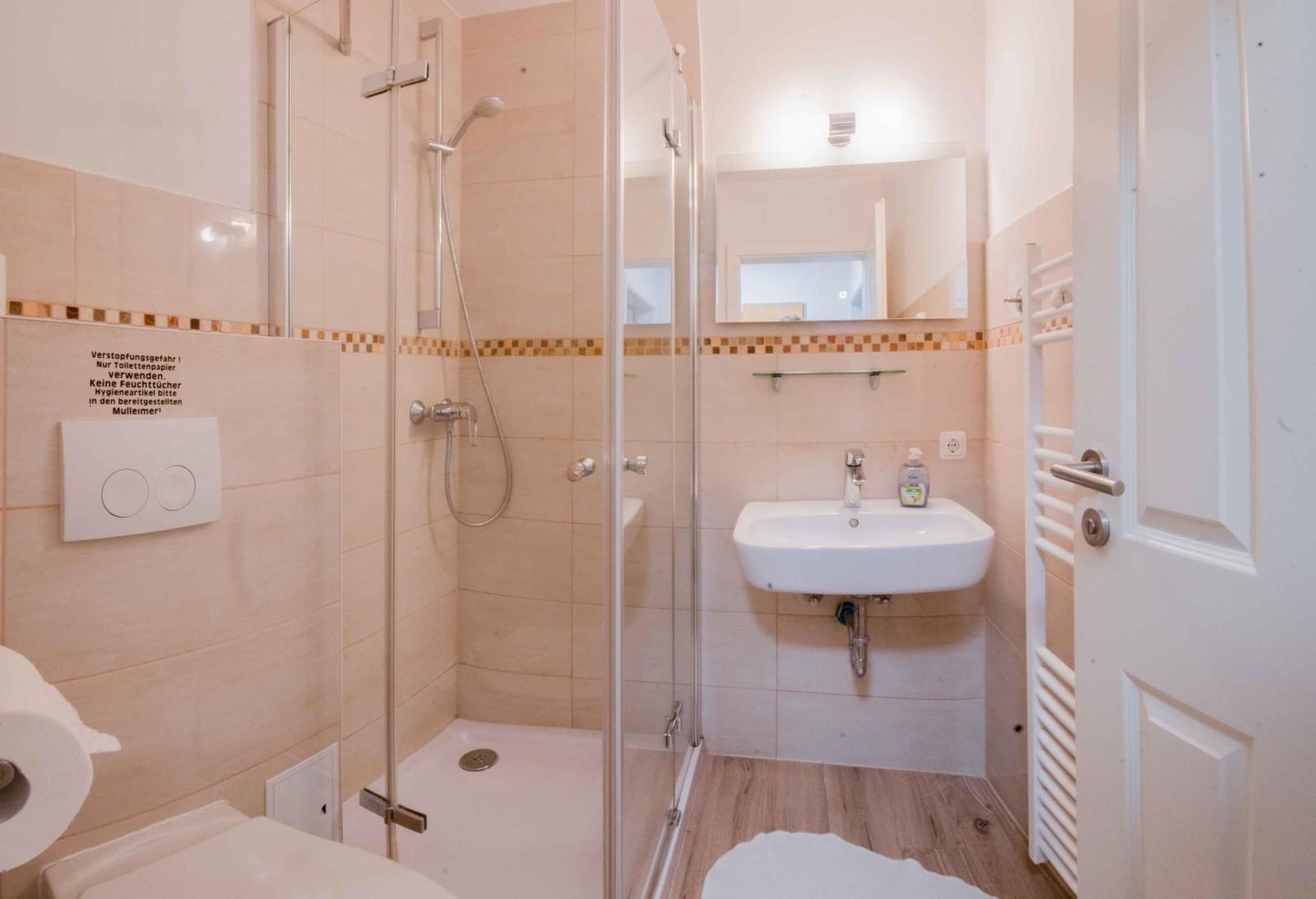 Badezimmer mit Dusche, Waschbecken und Toilette. Fliesenwand und Holzfußboden.