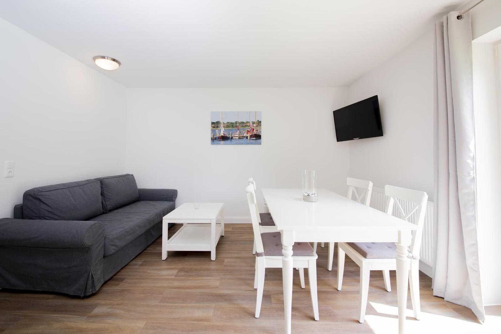 Wohn- und Essbereich mit Sofa, Esstisch, Fernseher und Wandbild.