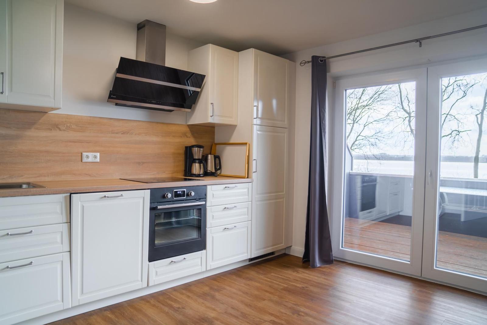 Küche mit weißen Schränken, Holzoptik und Blick auf Balkon.
