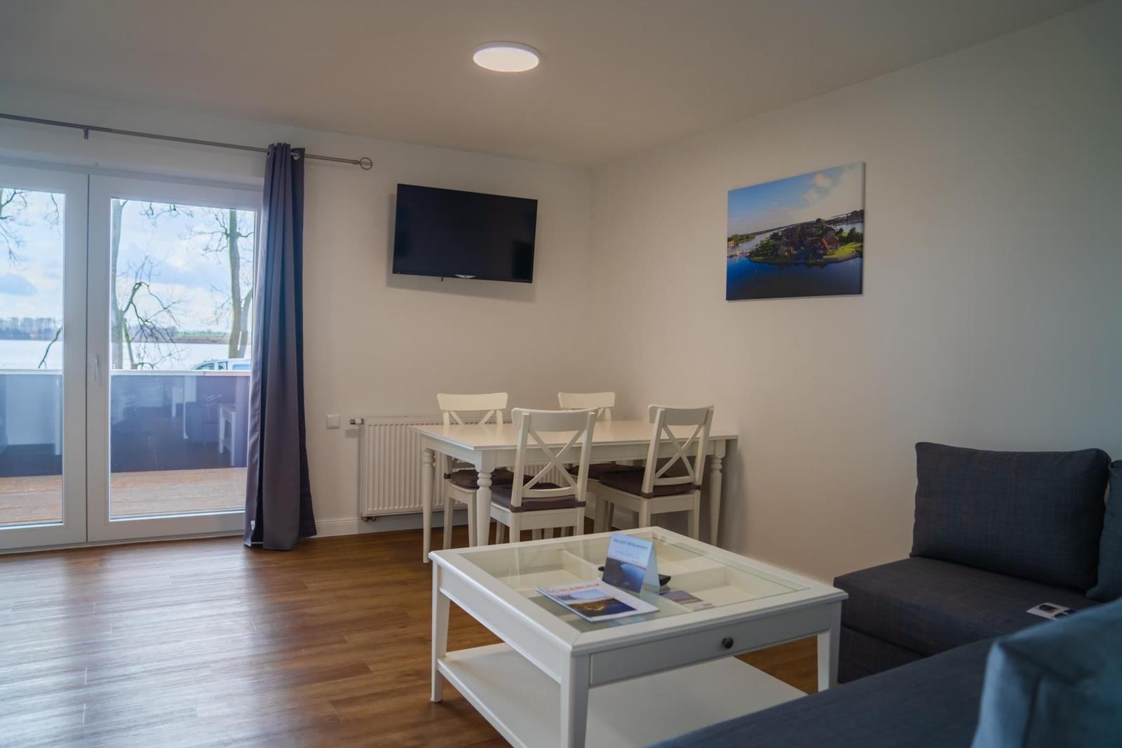 Wohn- und Essbereich mit TV, Tisch, Stühlen und Blick auf den Balkon.