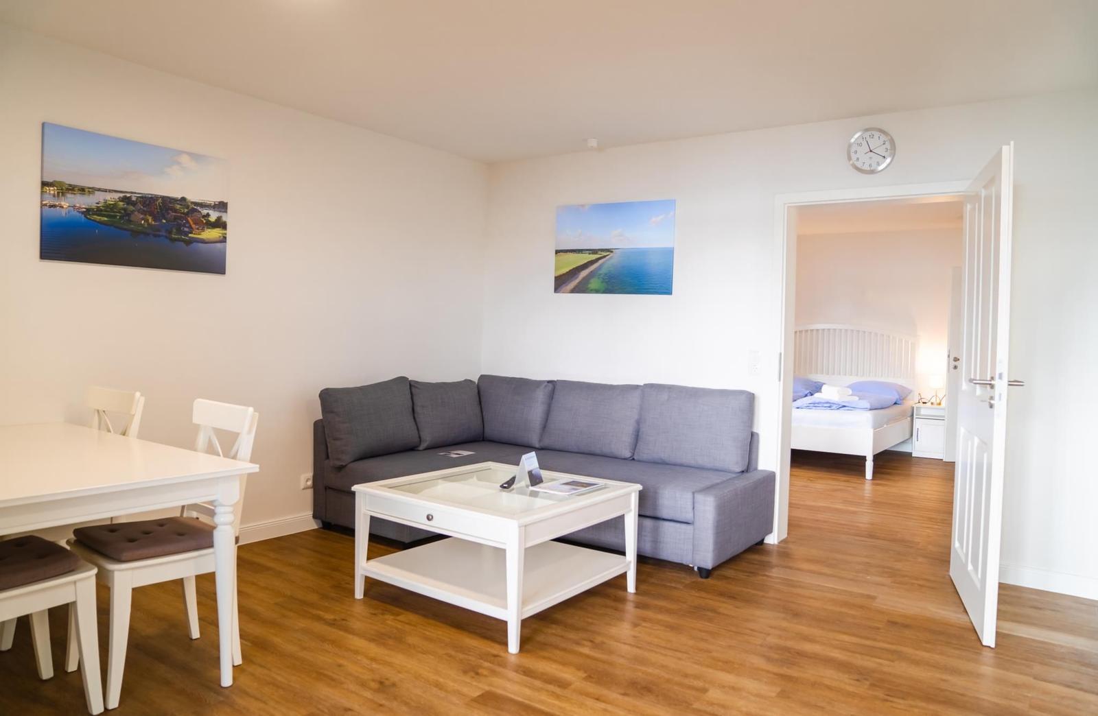 Wohn- und Essbereich mit Sofa, Tisch und Bildern an den Wänden. Durchgang zur Schlafzimmer.