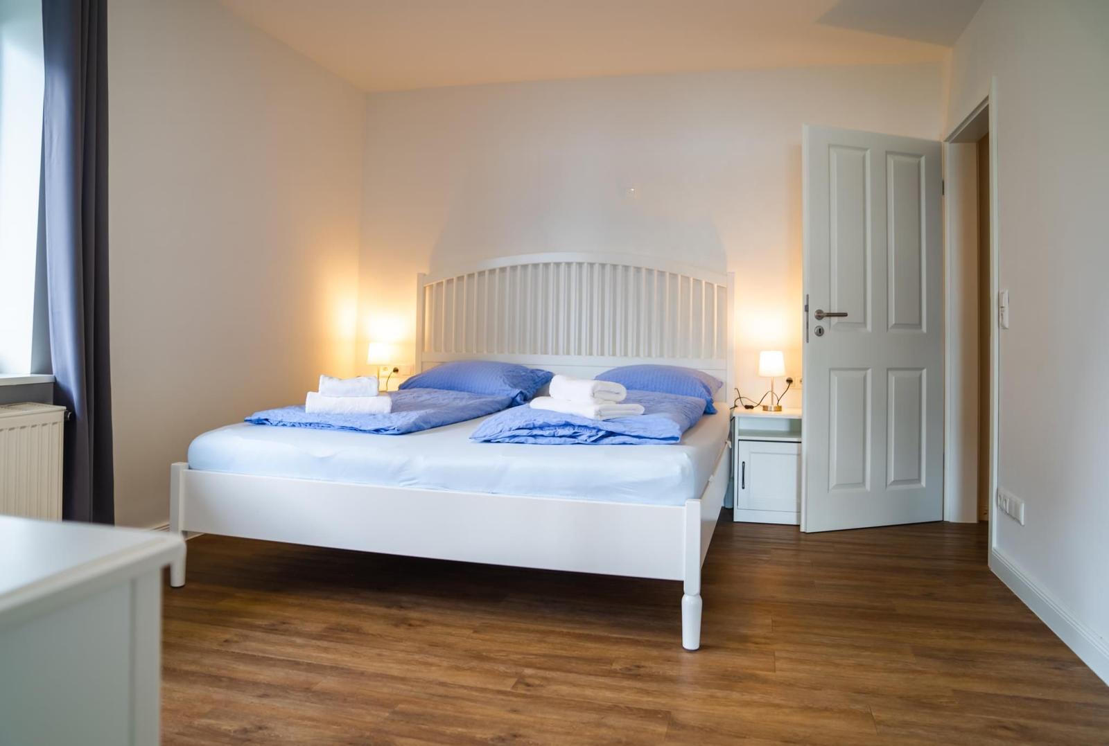 Schlafzimmer mit weißem Bett, blauer Bettwäsche und Holzboden.