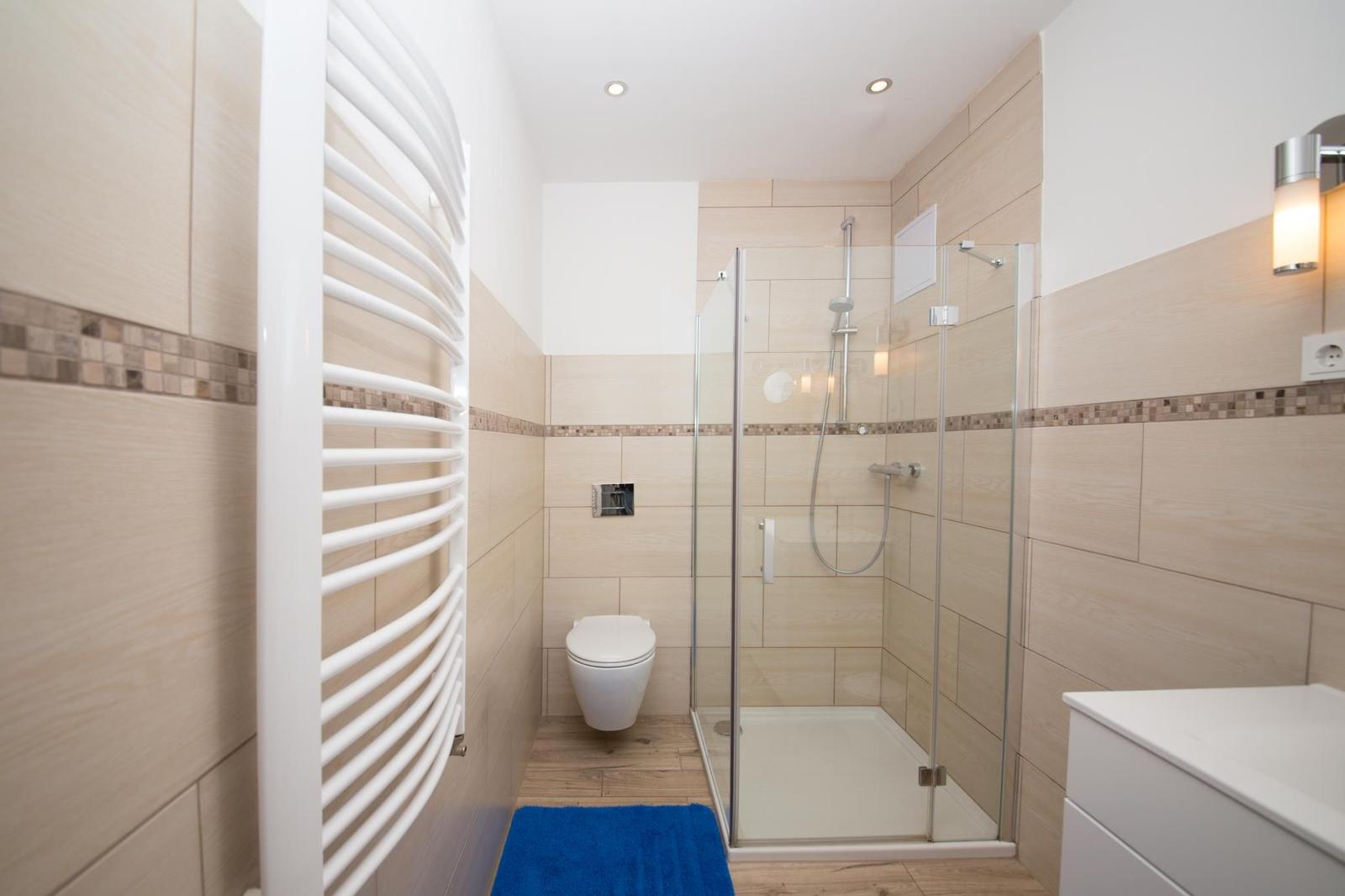 Badezimmer mit Dusche, Toilette und Heizung. Fliesenwand und Holzboden.