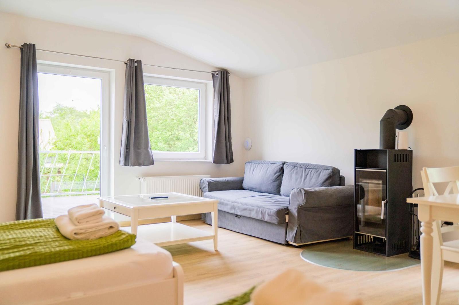 Wohnzimmer mit Sofa, Kamin und Blick auf Balkon mit grüner Umgebung.