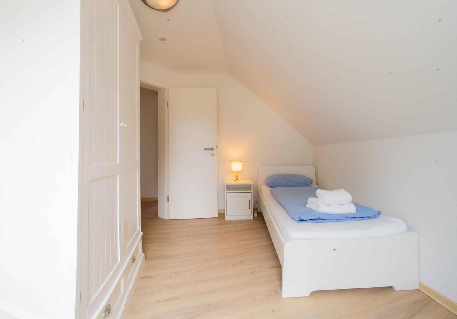 Schlafzimmer mit Einzelbett, Nachttisch und Kleiderschrank. Holzboden und schräges Dach.
