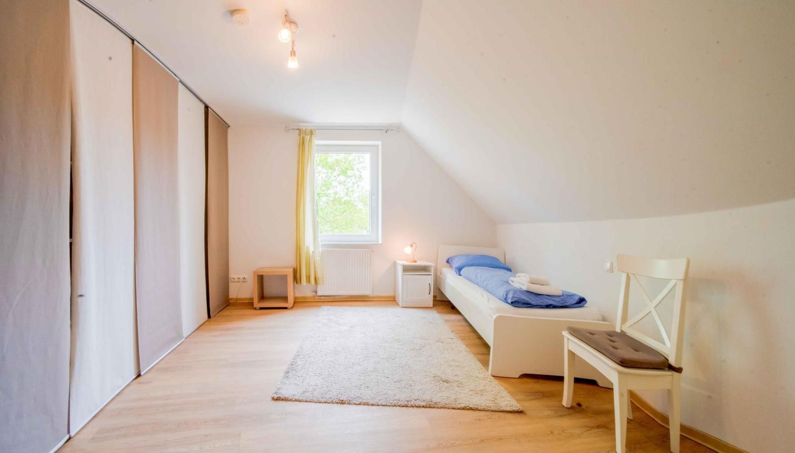 Ein Schlafzimmer mit Dachschräge, Bett, Stuhl und Schwebetüren.