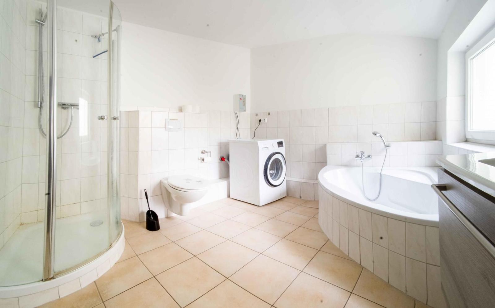 Badezimmer mit Dusche, Badewanne, Toilette und Waschmaschine.