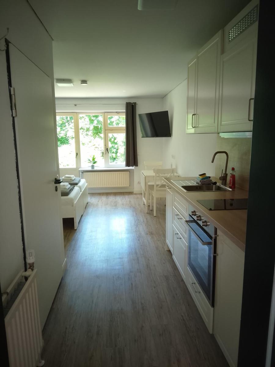 Küche mit Arbeitsfläche, Spüle und Herd. Wohnbereich mit Fenster und TV.