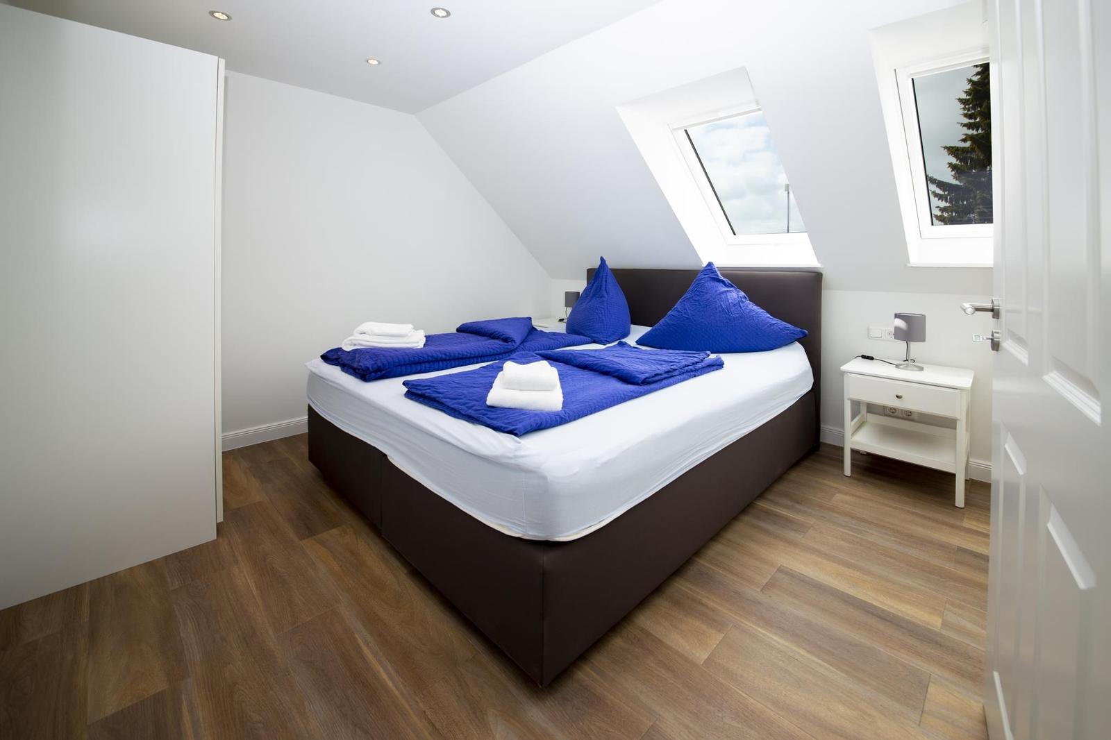 Schlafzimmer mit Dachschrägen, Bett mit blauer Bettwäsche und Holzboden.