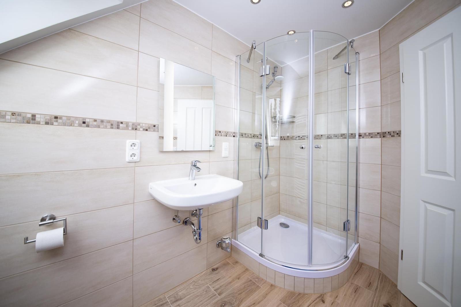 Badezimmer mit Dusche, Waschbecken und Spiegel an der Wand.