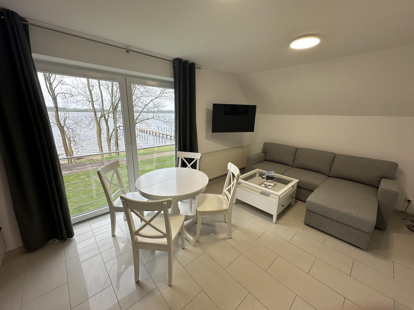 Wohn- und Essbereich mit Blick auf Wasser. Sofa, Esstisch und TV.