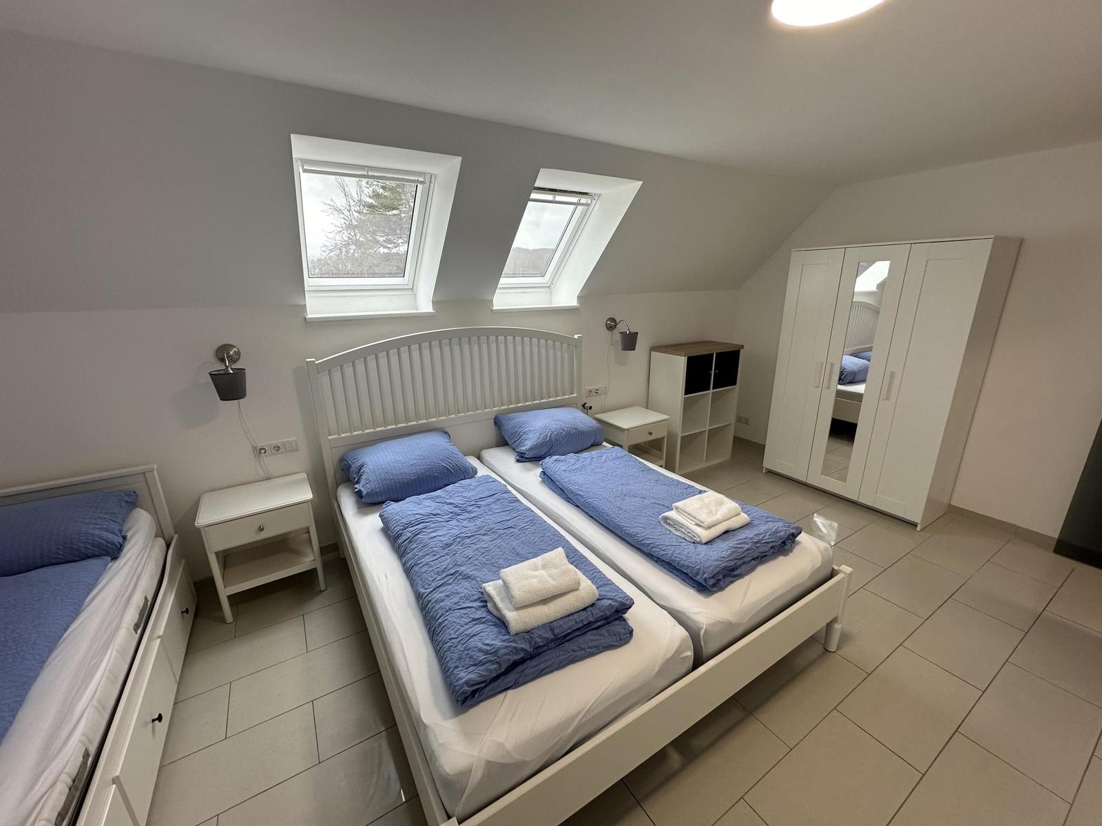 Schlafzimmer mit Doppelbett, zwei Dachfenstern und weißen Möbeln.