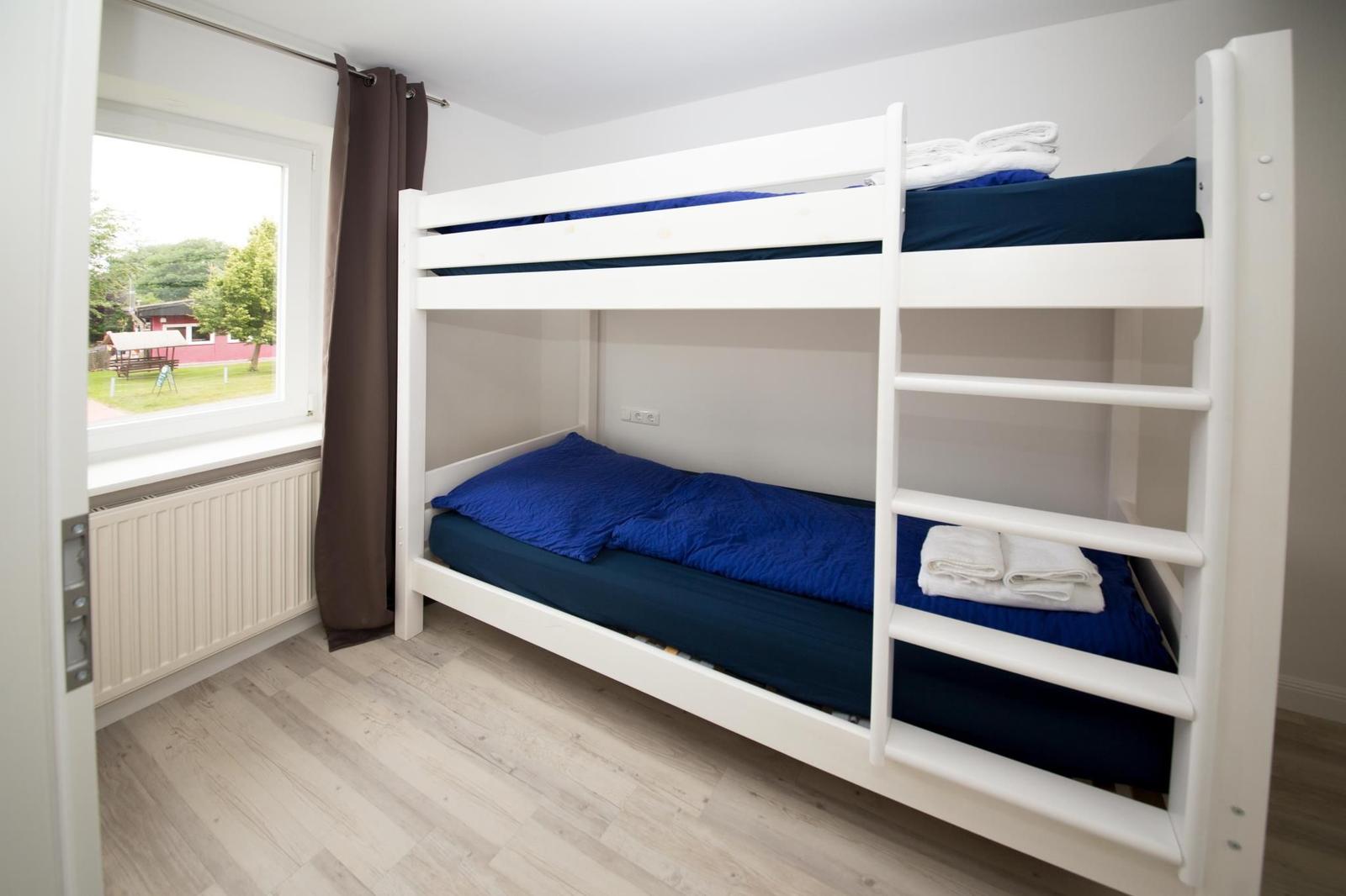 Zimmer mit Doppelstockbett, blauen Bettwäsche und Fenster mit Blick auf Garten.