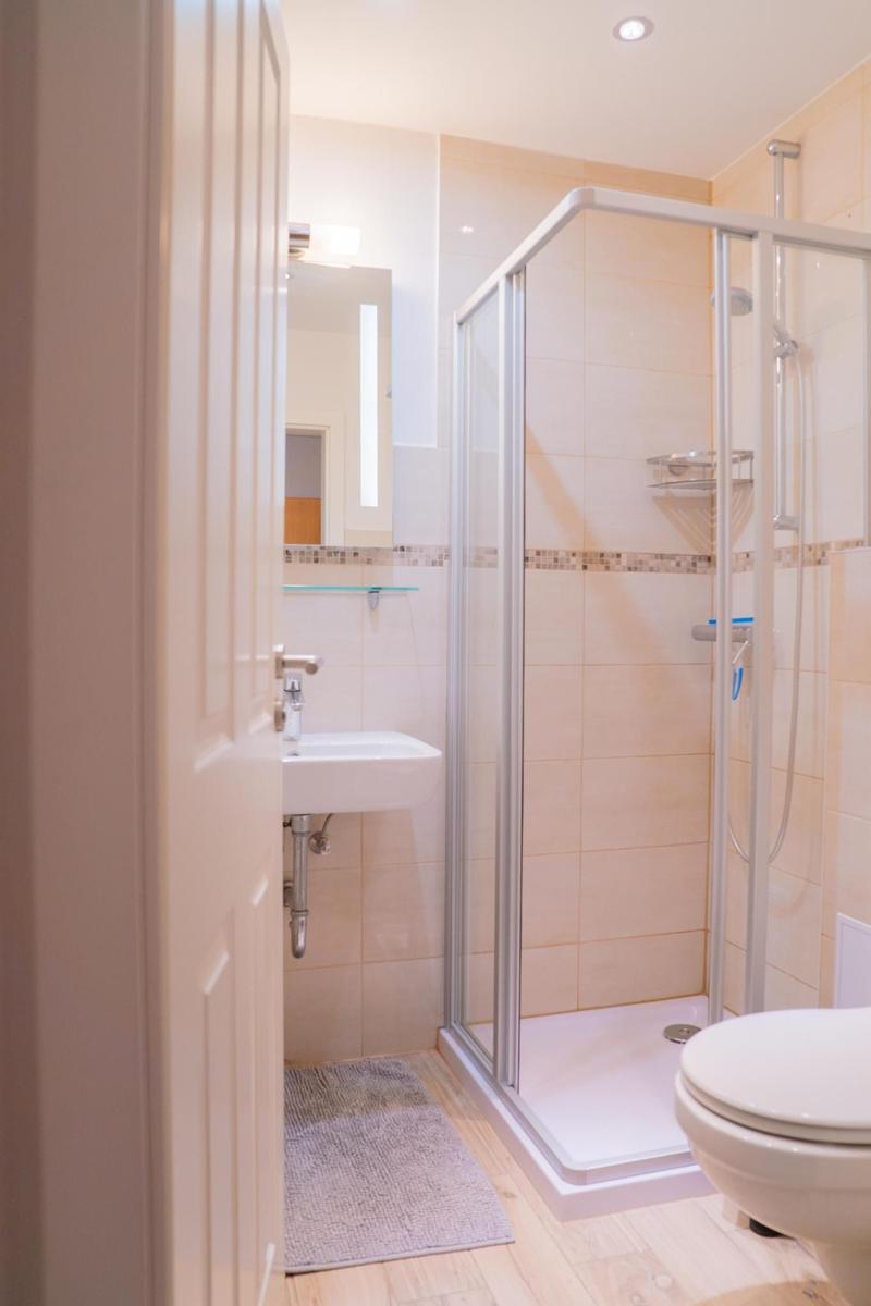 Badezimmer mit Dusche, Waschbecken und Toilette. Holzboden und Fliesenwand.