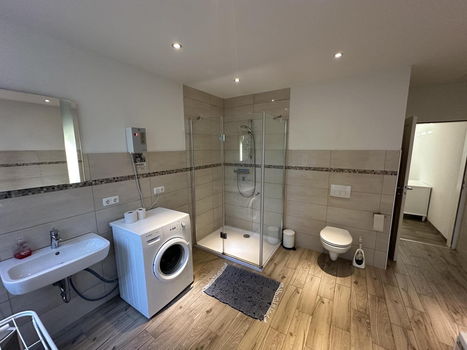 Badezimmer mit Dusche, Toilette, Waschmaschine und Spiegel.