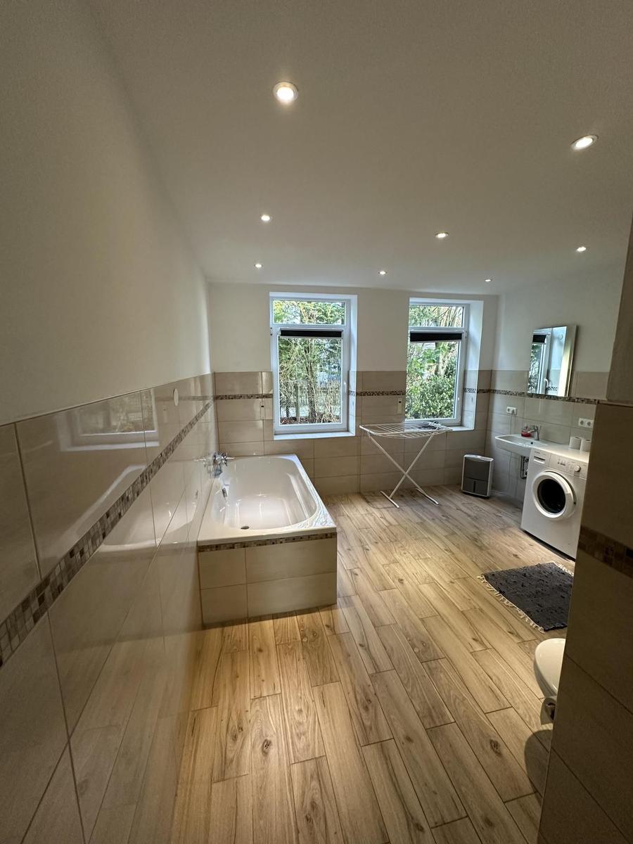 Badezimmer mit Badewanne, Waschmaschine und zwei Fenstern.