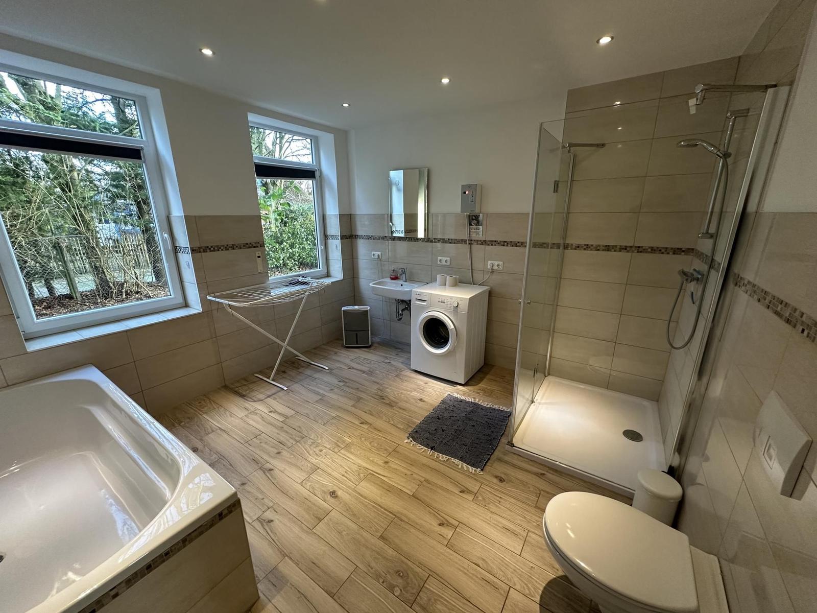 Bad mit Dusche, Badewanne, Waschmaschine und Fenstern.