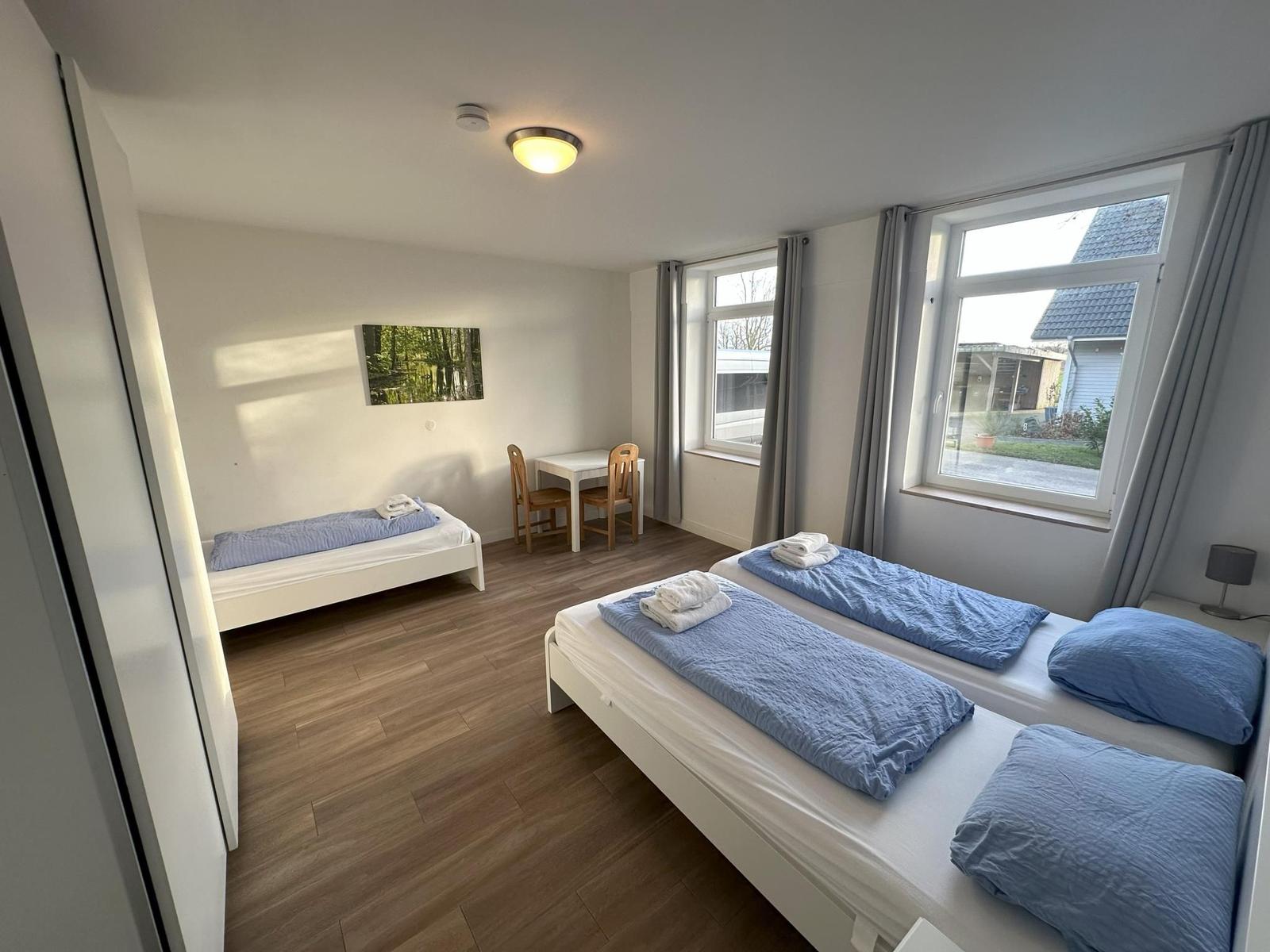 Zimmer mit zwei Betten, Tisch, Stühlen und Fenstern mit Blick nach draußen.