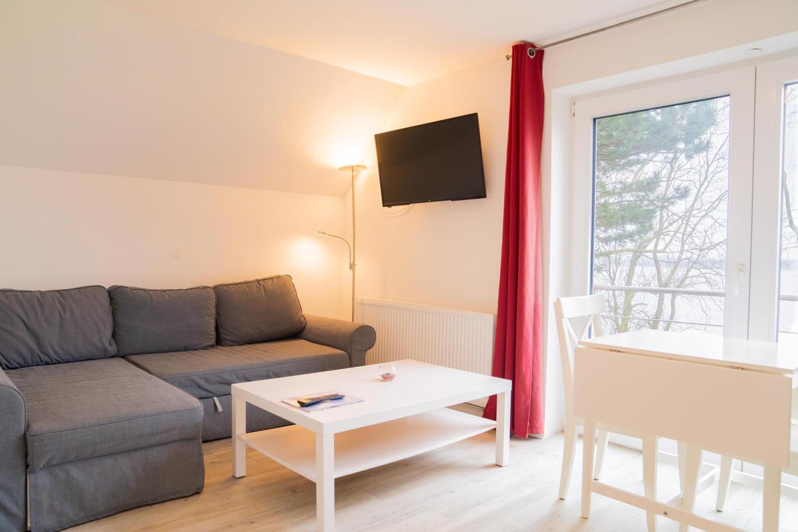 Wohnzimmer mit Sofa, Couchtisch und TV. Rote Vorhänge und Fenster mit Blick.