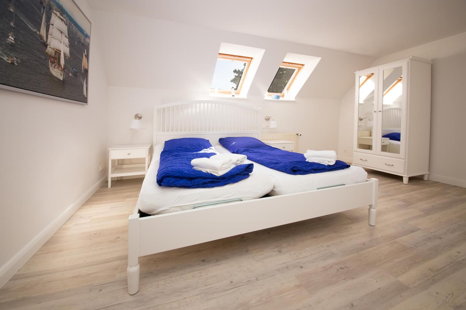 Schlafzimmer mit Doppelbett, blauer Bettwäsche, zwei Dachfenstern und weißem Schrank.