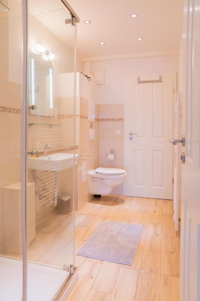 Badezimmer mit Dusche, Waschbecken und Toilette auf Holzboden.