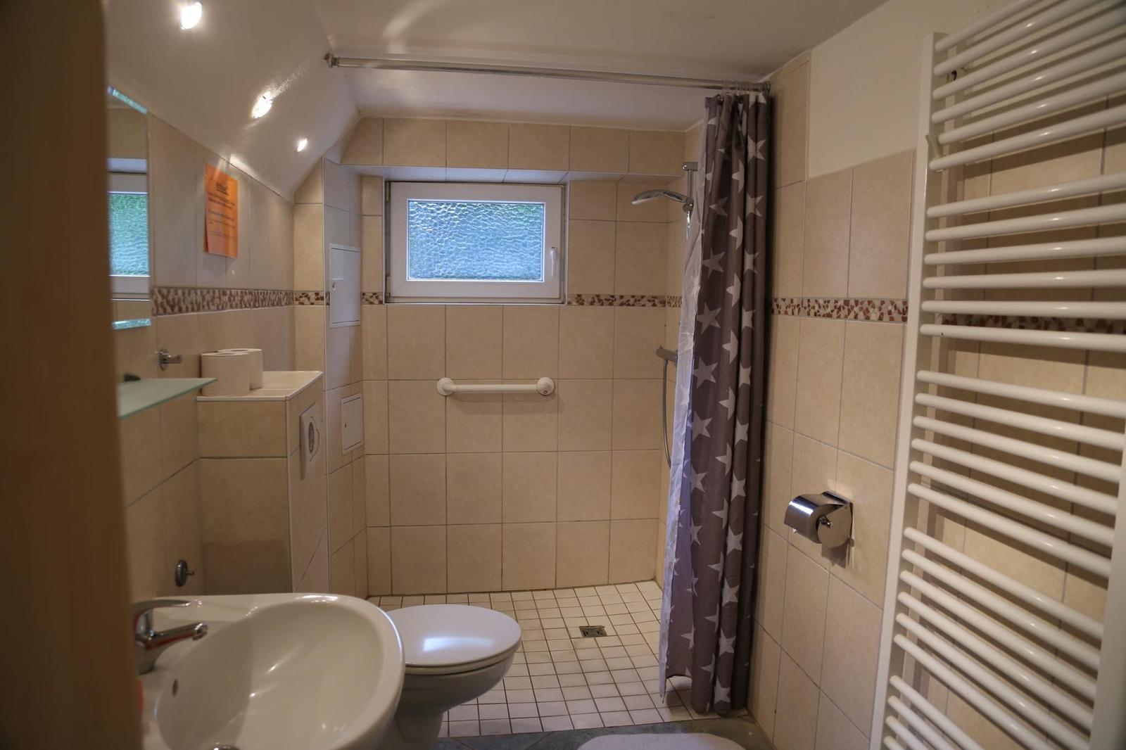 Badezimmer mit Dusche, Toilette und Waschbecken. Fenster und Heizkörper sichtbar.