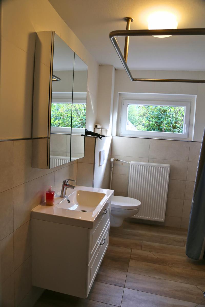 Badezimmer mit Waschbecken, Spiegelschrank, Toilette und Fenster mit Blick auf Grün.