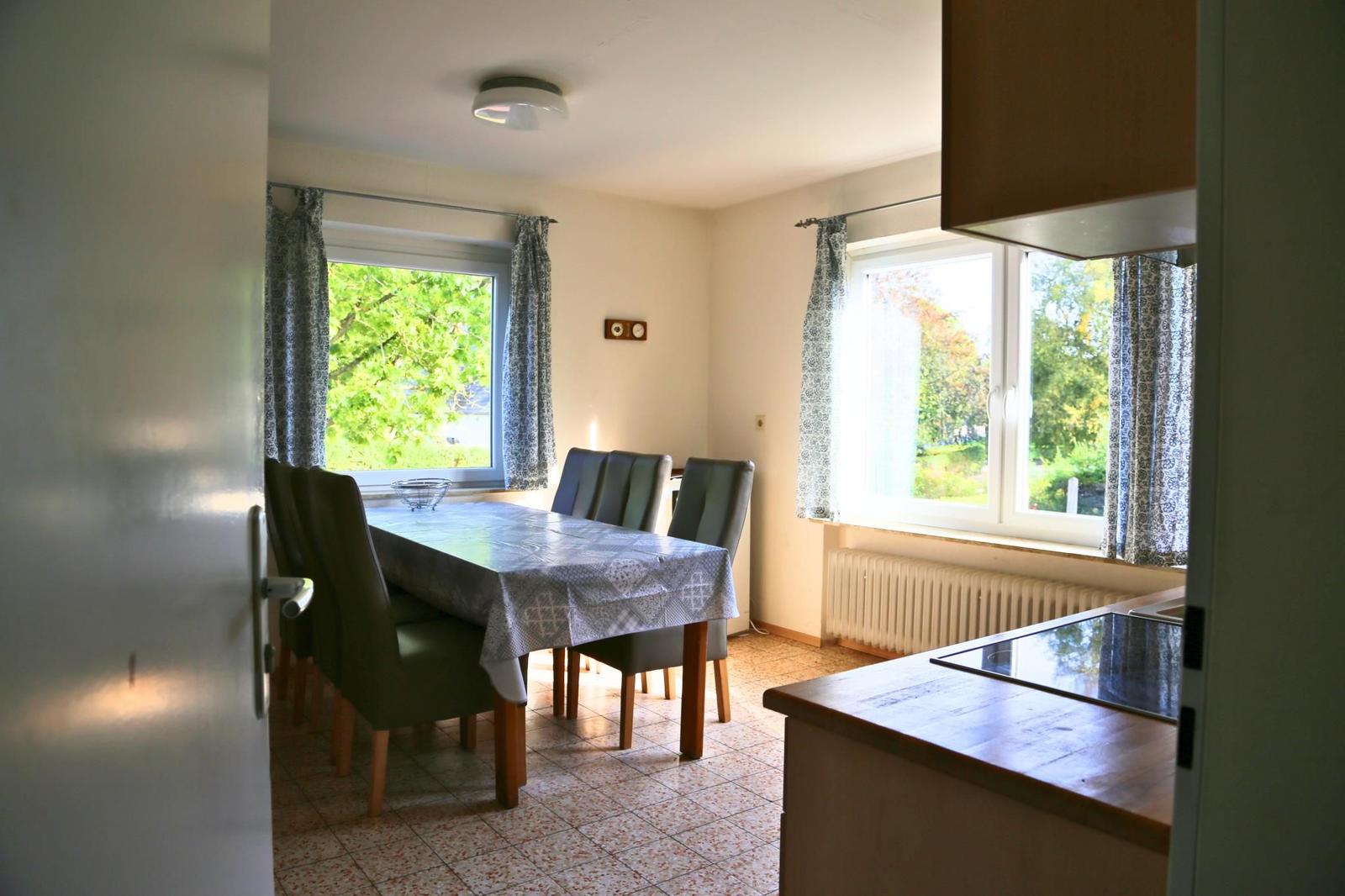Esszimmer mit Tisch, Stühlen und Fenstern. Kücheninsel im Vordergrund.