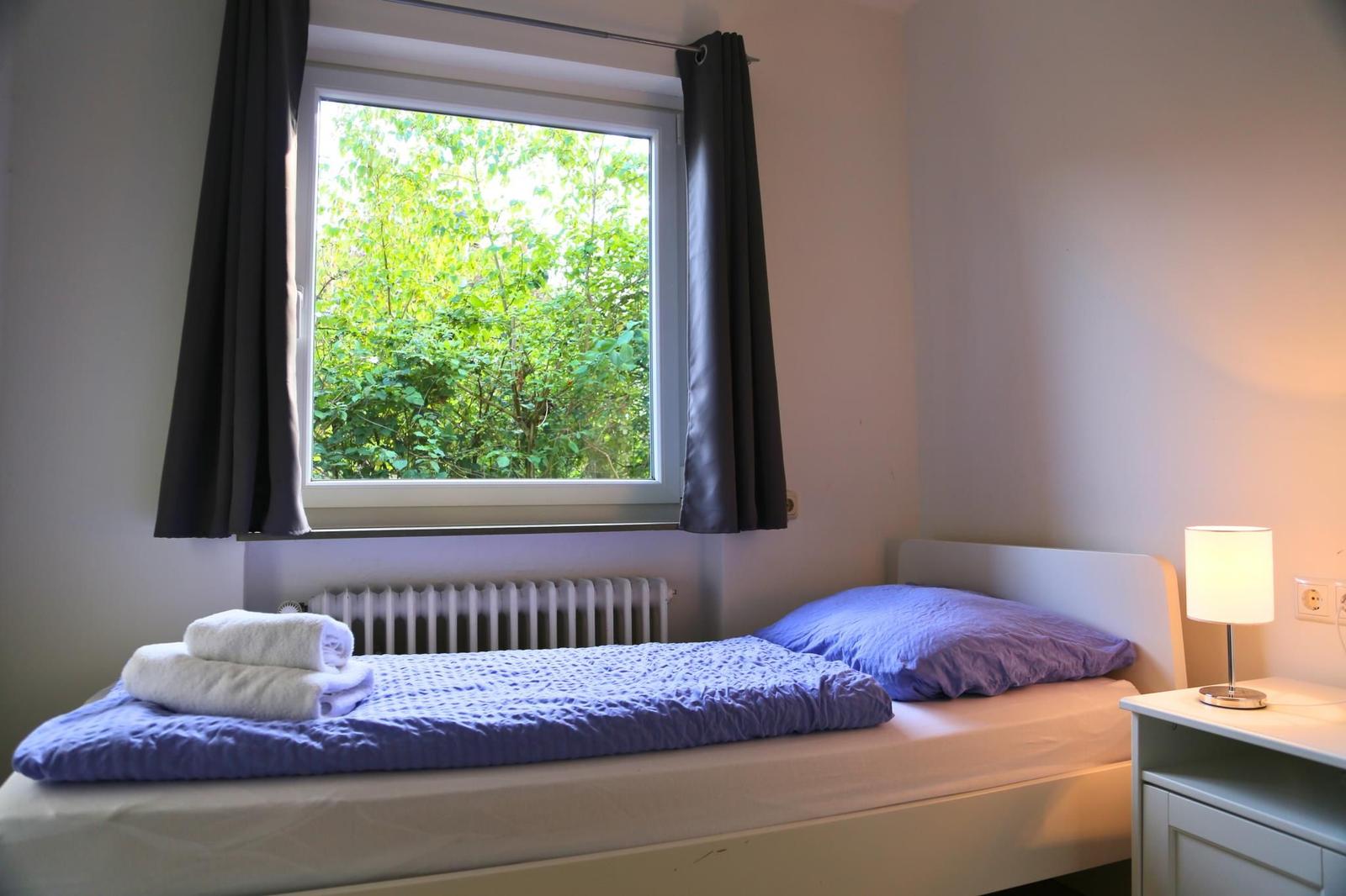 Ein Bett mit lila Bettwäsche und einem Fenster mit Blick auf Bäume.