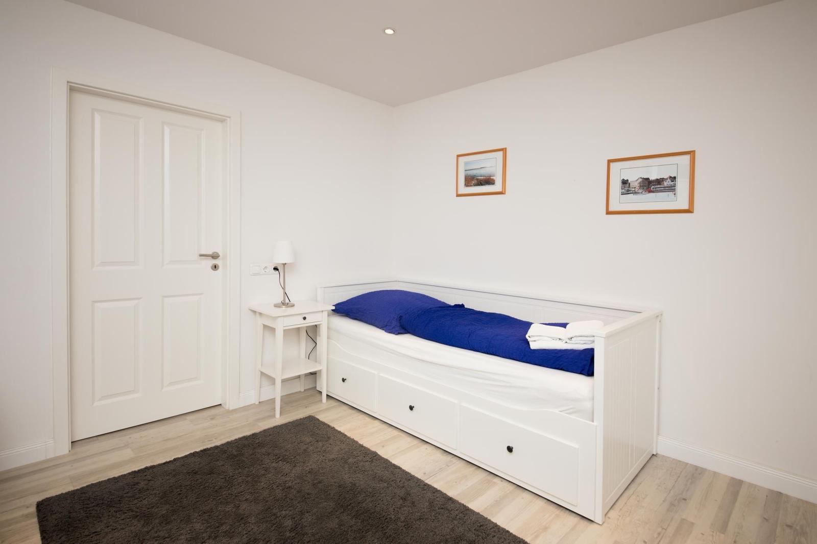 Schlafzimmer mit weißem Bett, Nachttisch und Bildern an der Wand.