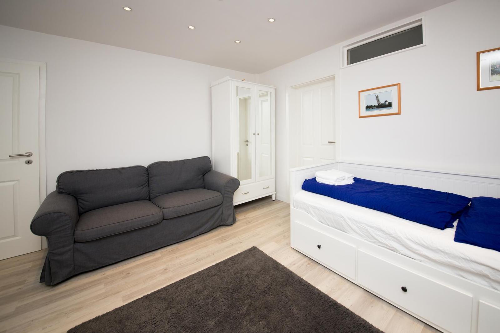 Zimmer mit Sofa, Bett und Kleiderschrank. Holzboden und weiße Wände.