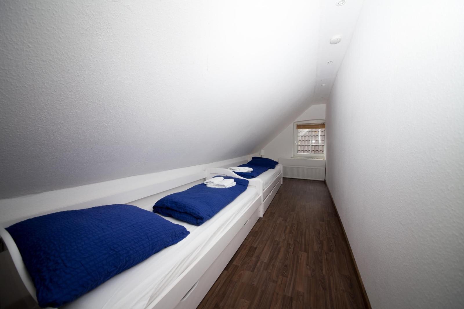 Zimmer mit drei Betten unter Dachschräge, Holzboden und kleinem Fenster.