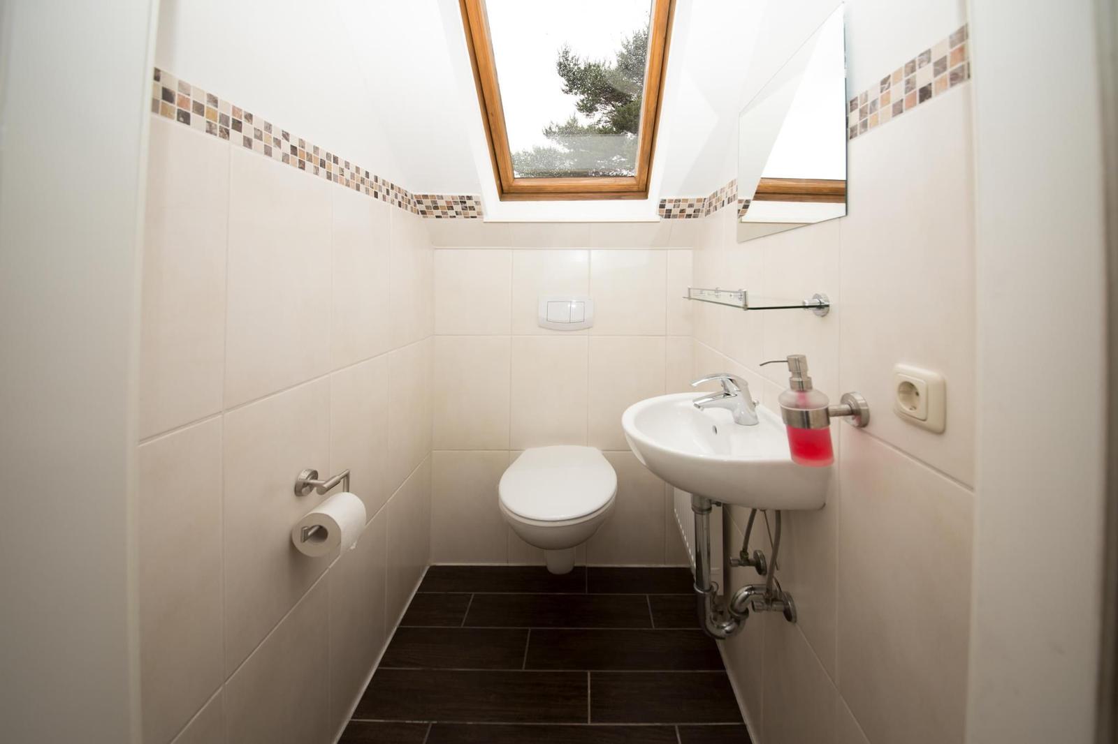 Badezimmer mit Toilette, Waschbecken und Dachfenster. Wandfliesen und dunkler Boden.