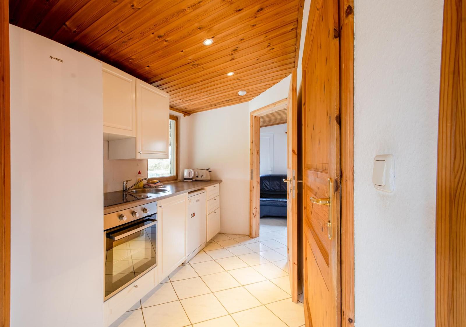 Küche mit Holzdecke, weißen Schränken und Blick in Wohnzimmer.