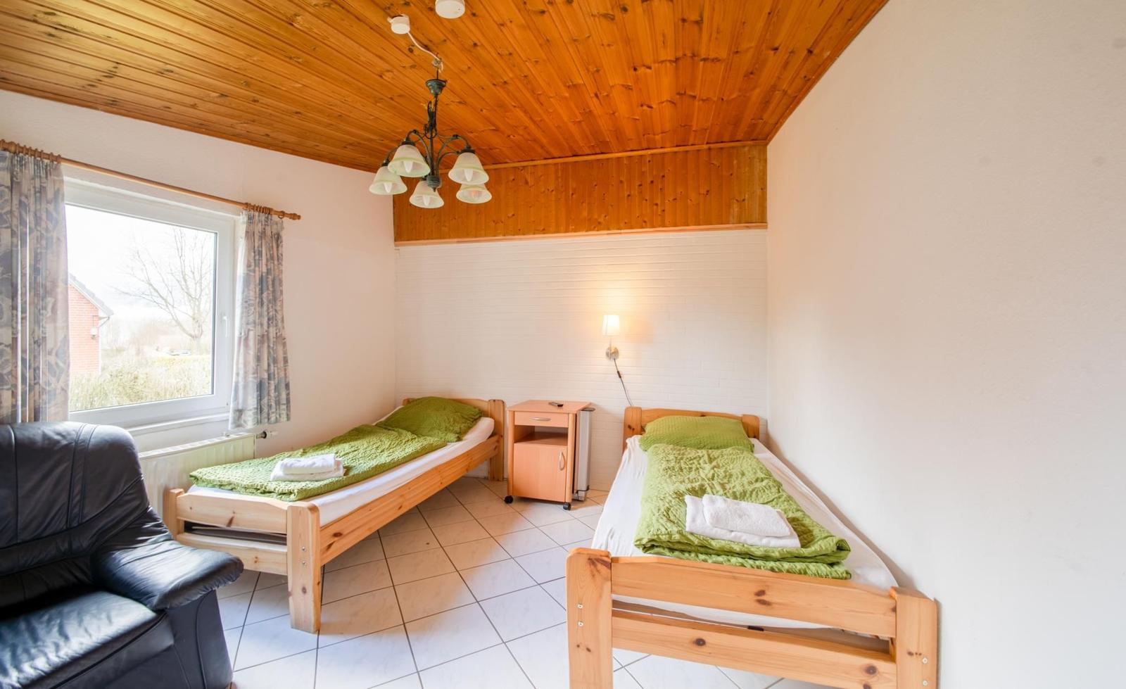 Zwei Einzelbetten mit grünen Bettwäschen, Holzdecke und Fenster mit Vorhängen.