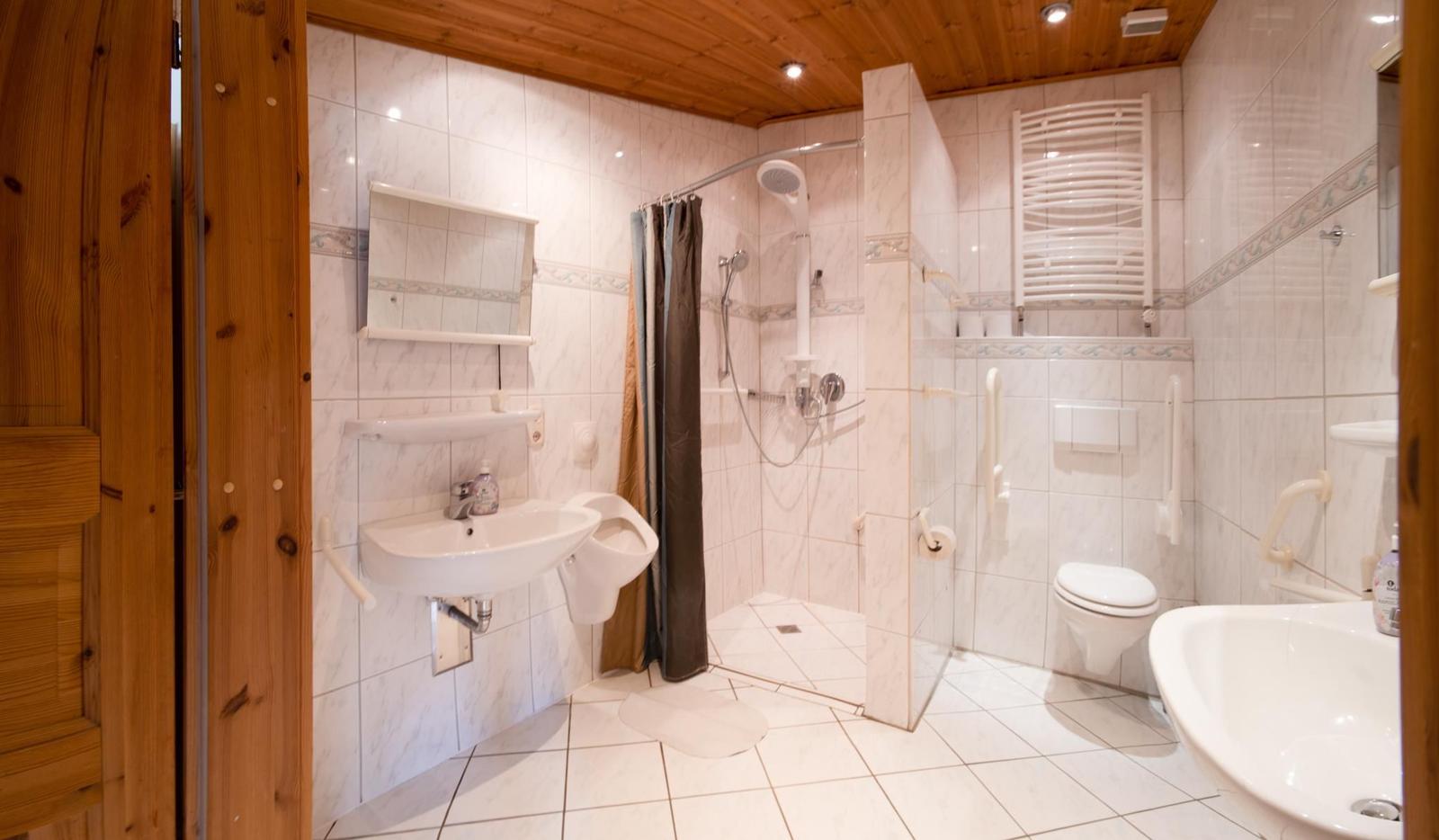 Bad mit Dusche, WC und Waschbecken. Holzdecke und Fliesenwand.