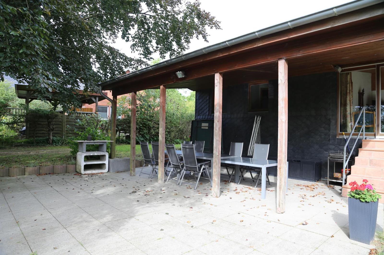 Terrasse mit Tisch, Stühlen und Grillplatz unter Dach