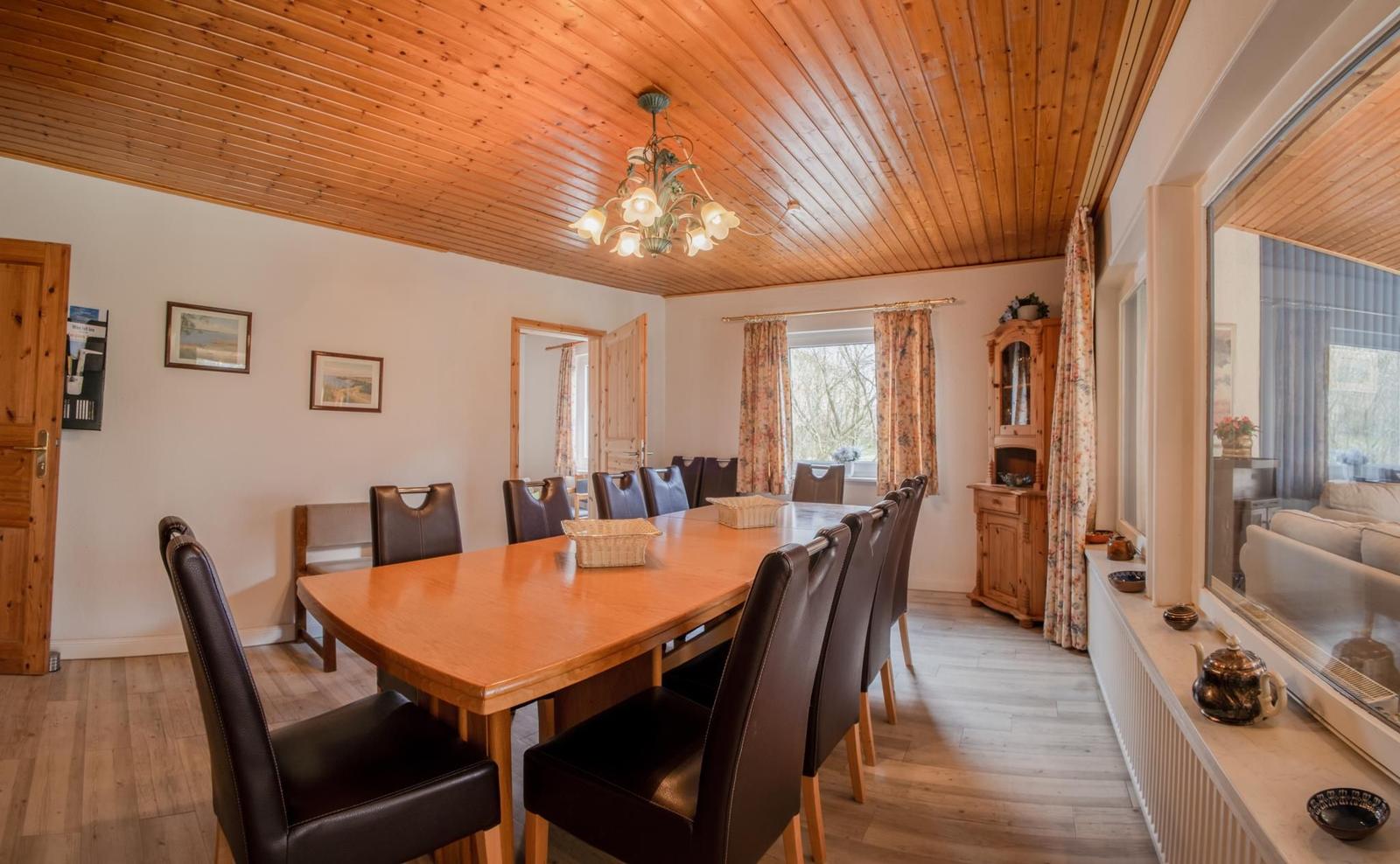 Esszimmer mit Holztisch, Stühlen und Fenster. Holzdecke und Sideboard sichtbar.