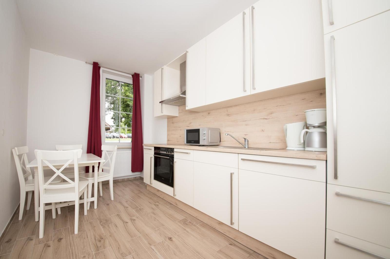 Küche mit Essbereich, weißen Schränken, Holzoberfläche und roten Vorhängen an Fenster.