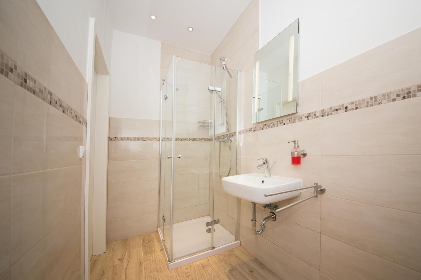 Badezimmer mit Dusche, Waschbecken und Spiegel.